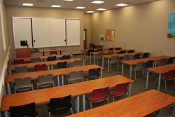 A view from the back of the room of the rows of red and black chairs and wooden tables in the Milham Room.